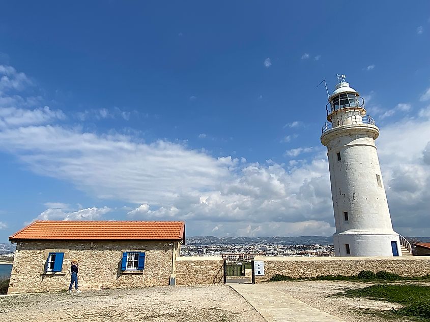 A woman takes a picture of a white lighthouse tower standing beside the brick light keeper's house