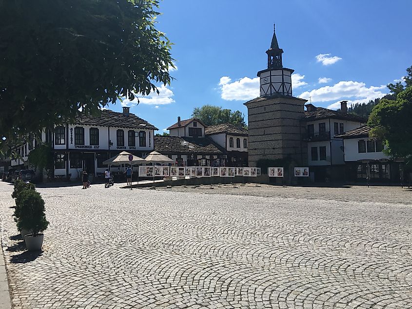 A clock tower stands at the center of a spacious, cobblestone town square.
