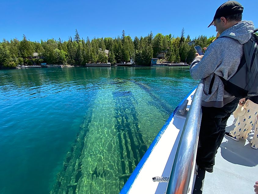 A man aboard a cruise boat photographs a shipwreck seen just below the surface of a shallow harbour.