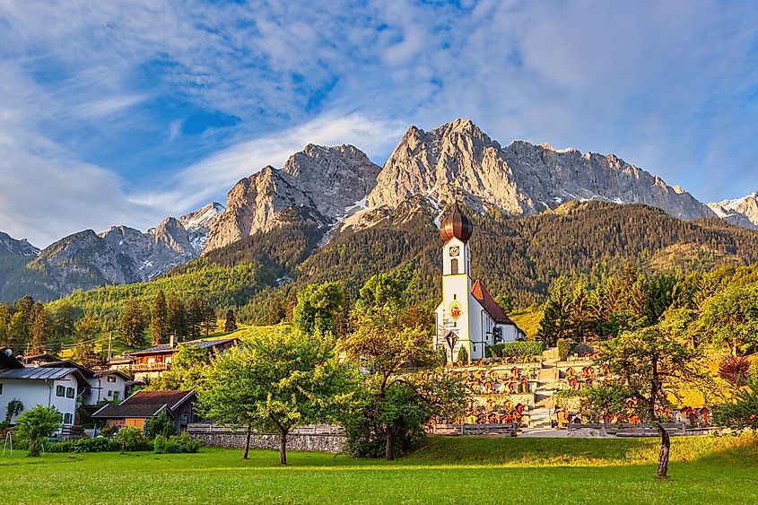 Zugspitze peak and Alps mountain range in Garmisch Partenkirchen, Germany, with a village church in Grainau.