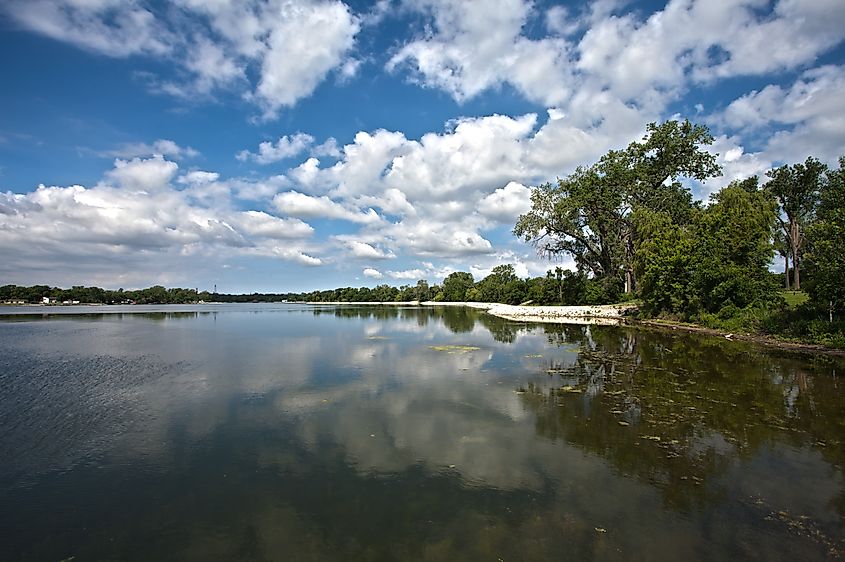 Carter Lake in Iowa, featuring pretty clouds reflected in the water and surrounded by lush trees along the shoreline.