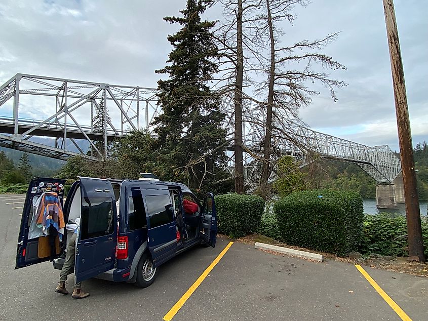 A blue van with all doors open is parked under the steel, Bridge of the Gods in Cascade Locks, Oregon. 