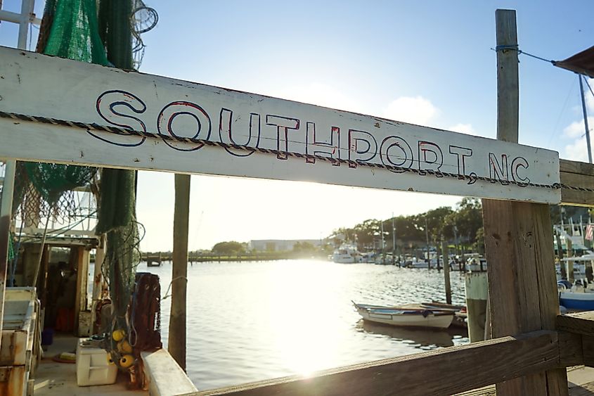 A weathered Southport, NC sign hangs at a dock in front of a fishing boat on the Cape Fear River