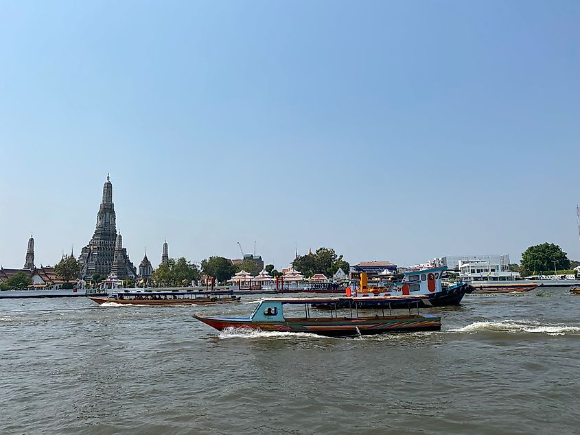 Long boats criss crossing the main river in Bangkok. The impressive pagoda of Wat Arun can be seen in the distance.