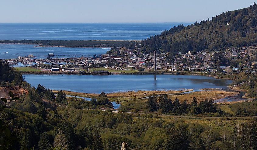 Overlooking a coastal town surrounded by lush hills and a large, reflective lagoon, with the expansive blue ocean in the background under a clear sky.