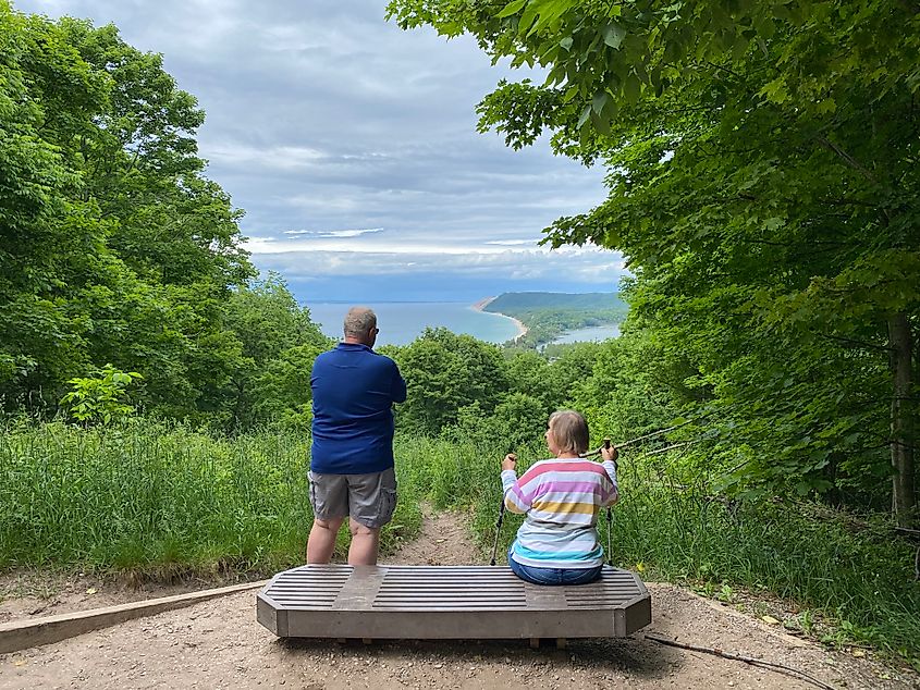 An elderly couple takes a break from hiking at a bench overlooking Michigan's sandy and forested Sleeping Bear Dunes National Lakeshore.