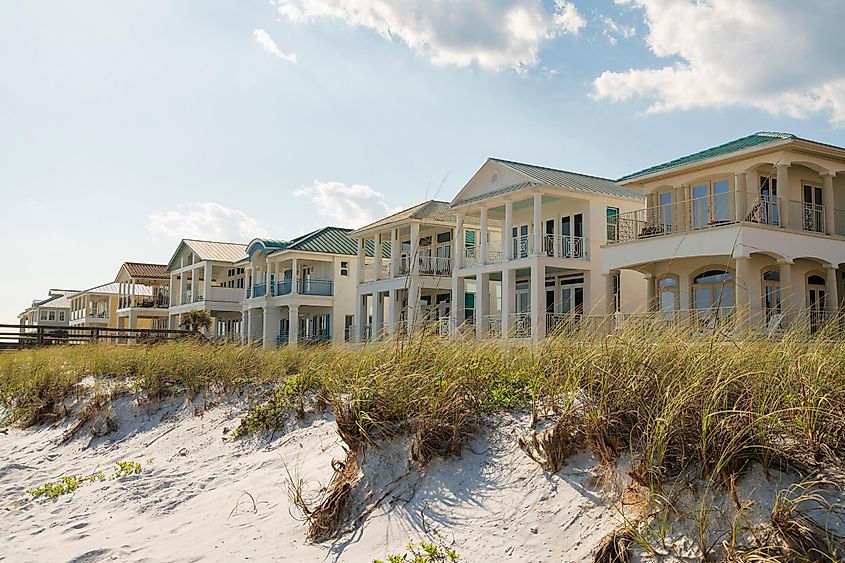 White sand dunes with tufts of grass foregrounding multistory beach houses with balconies in Destin, Florida