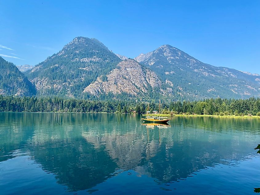 A serene reflection on Lake Chelan in North Cascades National Park, with towering mountains and lush forests mirrored on the calm water.