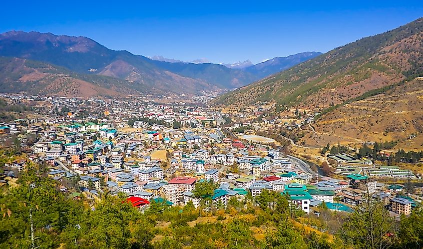 Aerial panoramic view of Thimphu capital city set in a mountain valley with colorful buildings and snow-capped Himalayan peaks in Bhutan