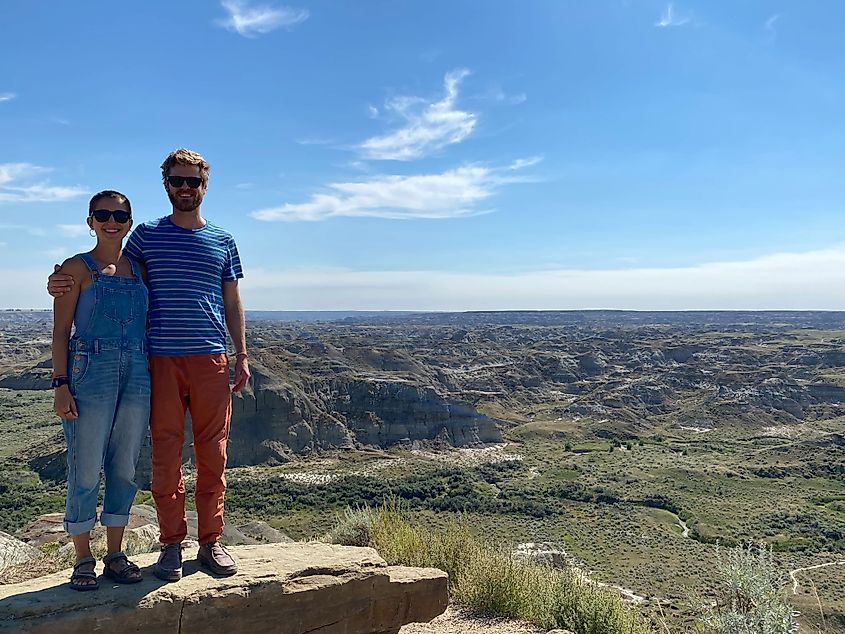 A young, smiling couple poses at a viewpoint above the badlands of Alberta's Dinosaur Provincial Park