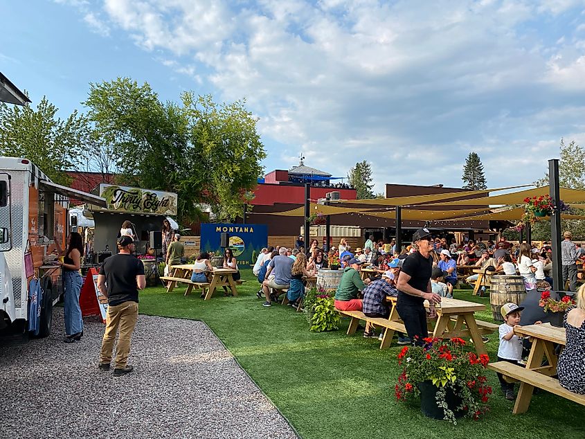 A large crowd fills almost every picnic table within an outdoor venue with food trucks around the perimeter.