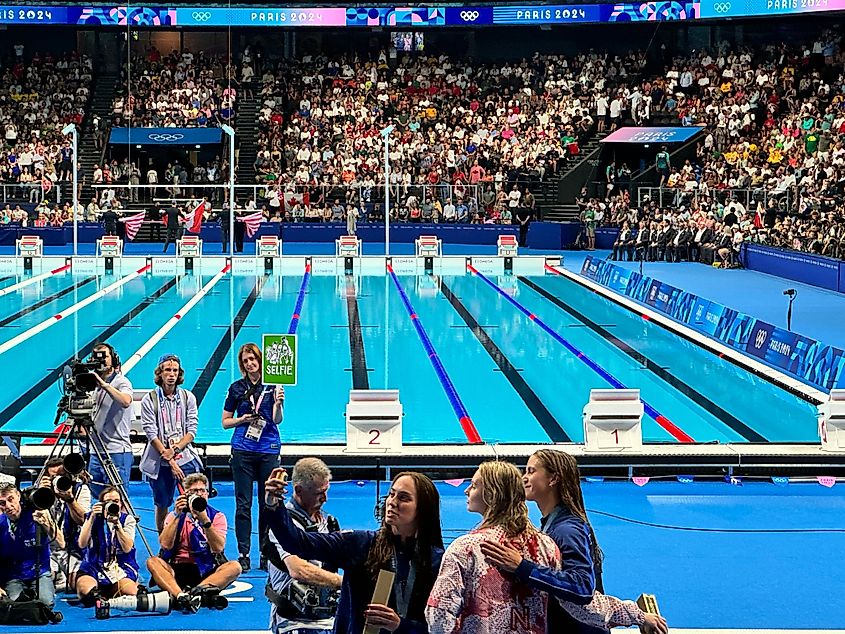 Olympics employee holding "Selfie" sign while women swimmers who won medals take a group selfie at Paris La Defense Arena during the Summer Olympics. Editorial credit: Here Now / Shutterstock.com