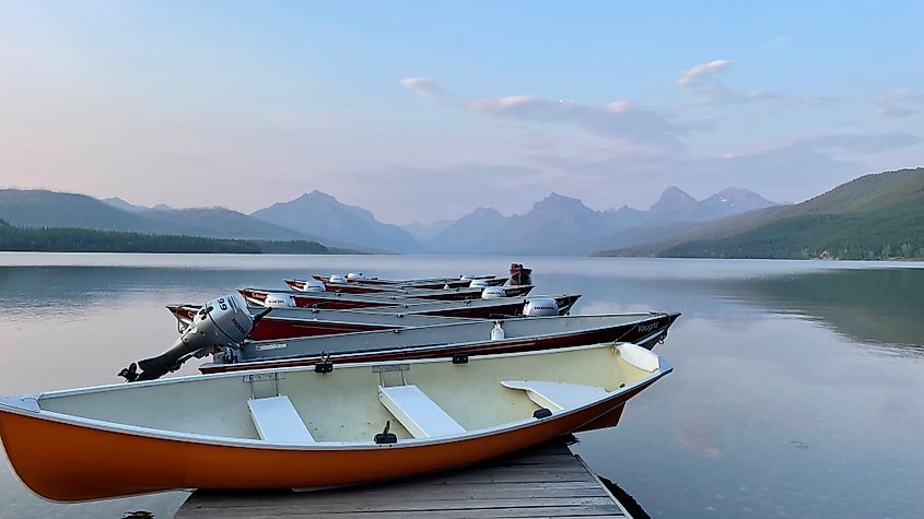 Red boats stacked neatly on a dock at Glacier National Park's Lake McDonald. A pastel evening sky and Rocky Mountain peaks make for a picture-perfect scene.