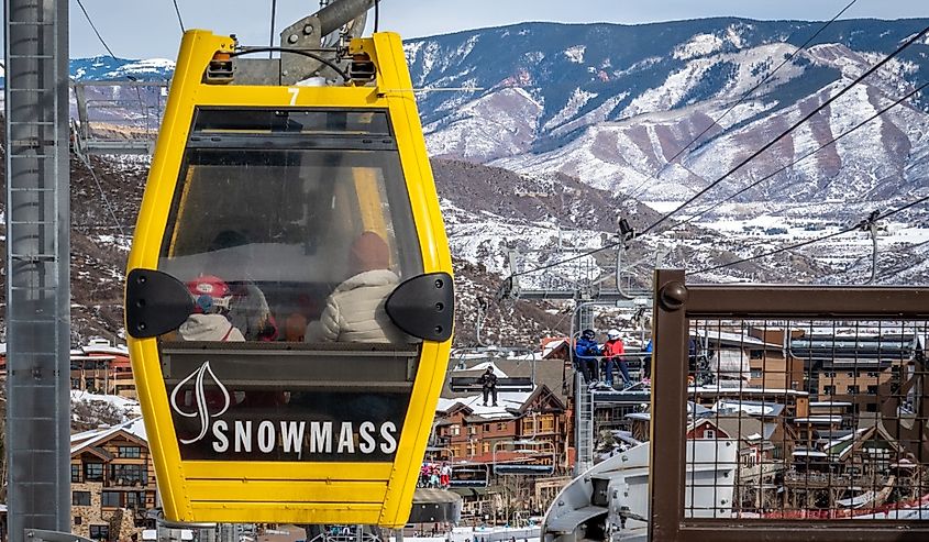 A gondola known as the "Skittles" people mover transports people from the Base Village to the Snowmass Mall, with Rocky Mountains in the background.