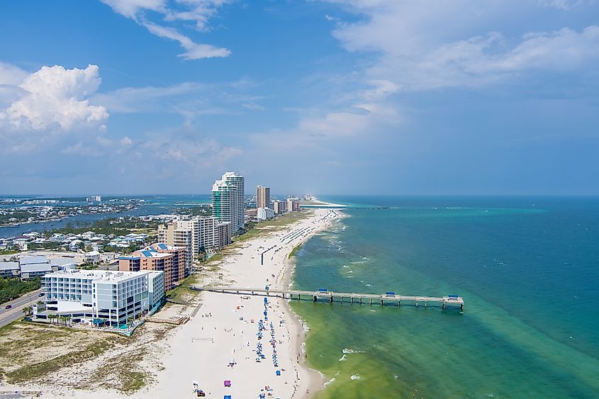 Aerial view of the beach at Orange Beach, Alabama, on a sunny day in July, featuring the sandy shoreline, blue ocean, and beachgoers enjoying the warm weather.