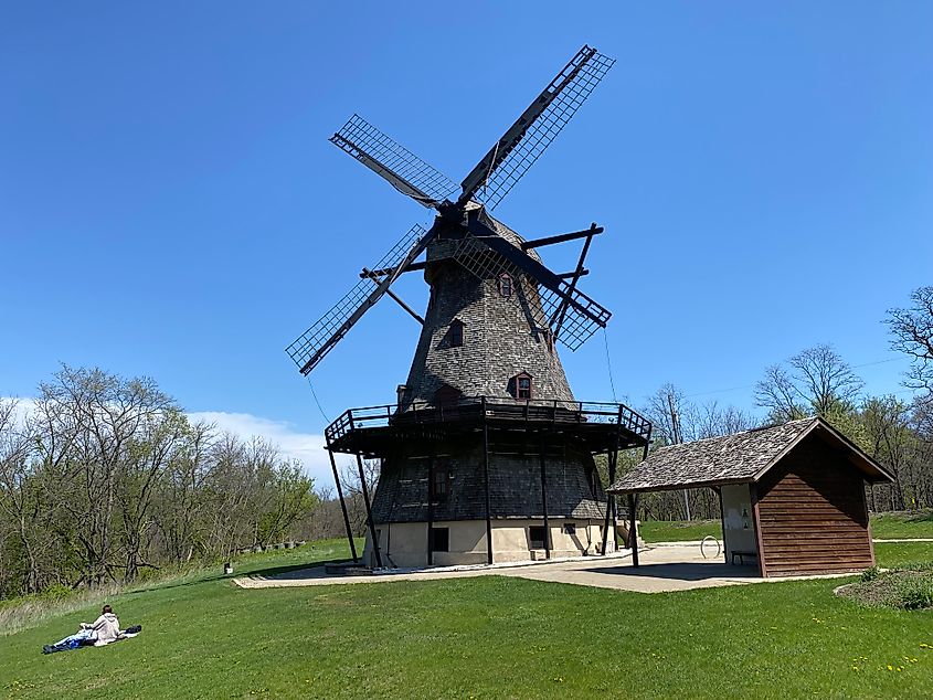 A couple lays in the grass before a large Dutch windmill.