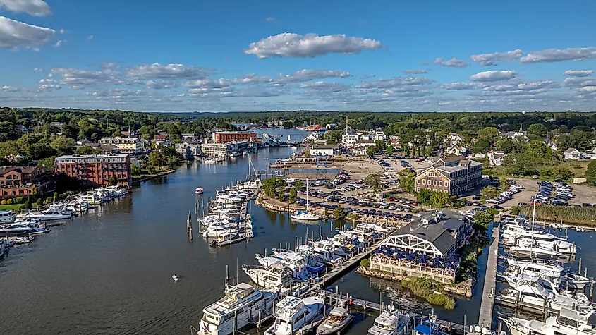 Aerial view of Mystic, Connecticut with boats docked along the Mystic River, waterfront buildings, a marina, and a bascule bridge in the distance.