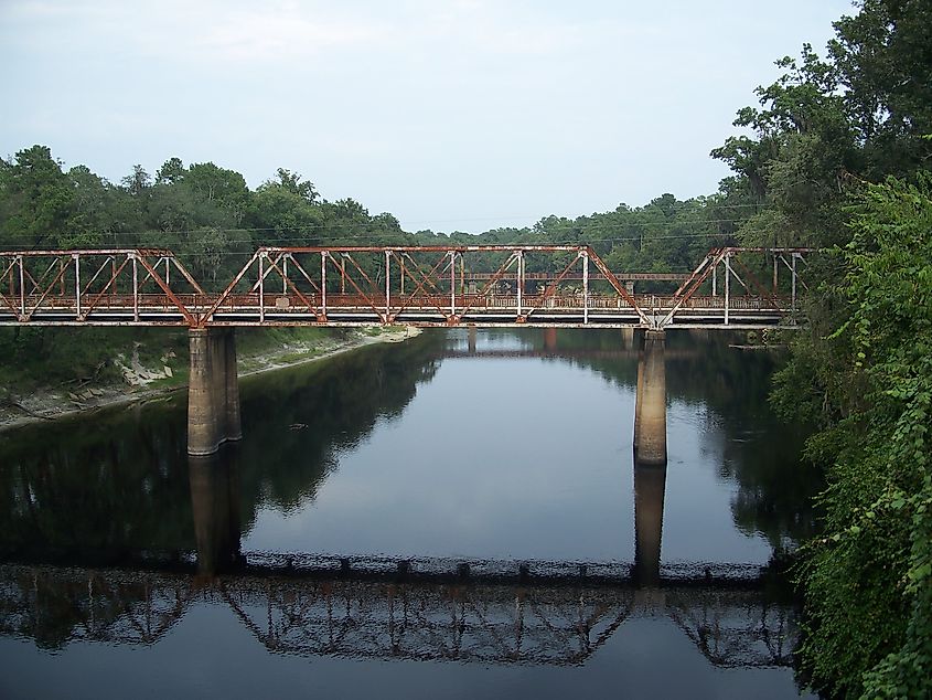 Suwanee River with the old steel truss US90 bridge reflected in it and a railroad bridge behind it.