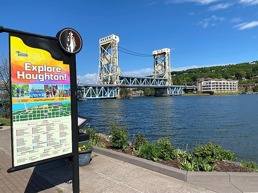 A welcome sign for the town of Houghton, Michigan stands in front of a large canal lift bridge. 