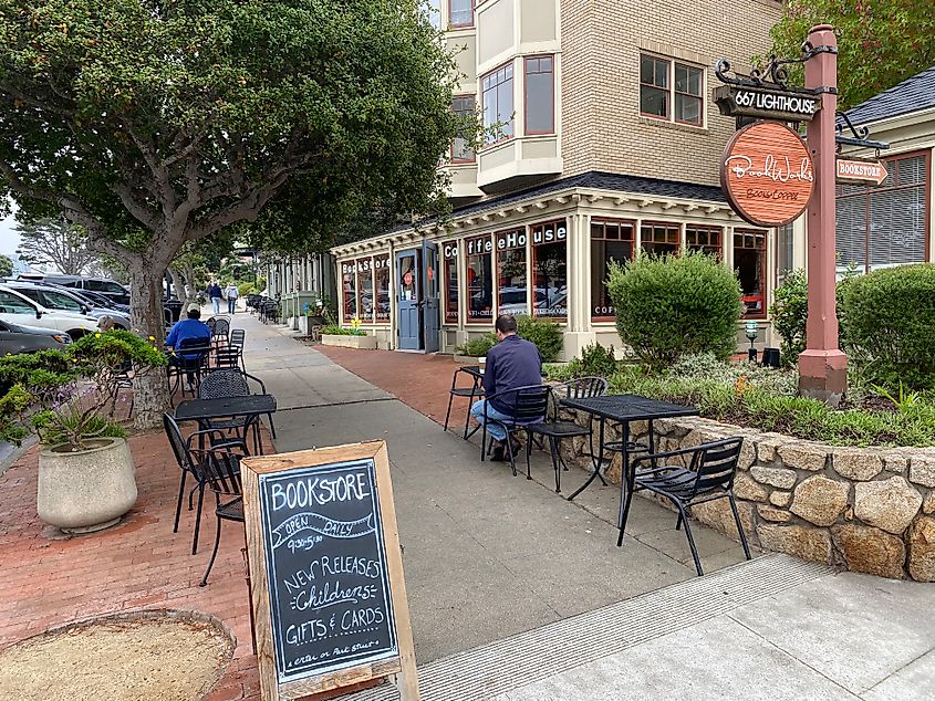 A couple men sit at different sidewalk tables outside of a bookstore/coffee shop.