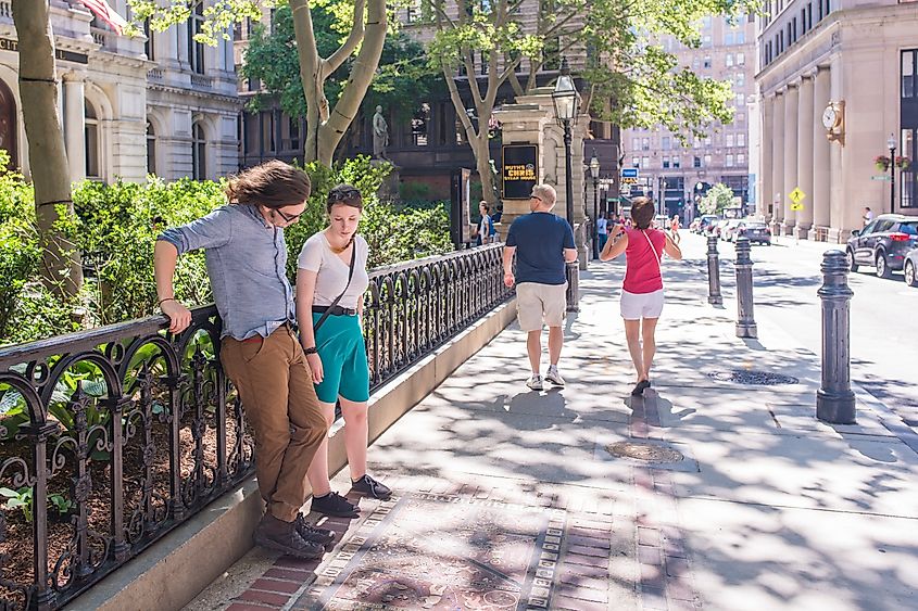 Tourists stop to look at a stone monument on the ground at the site of the oldest school in America, a stop along the Freedom Trail. Editorial credit: Page Light Studios / Shutterstock.com