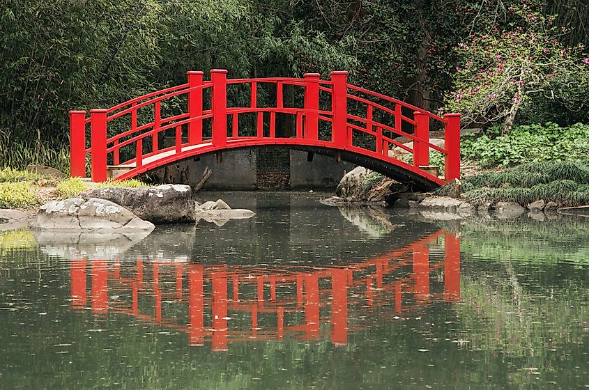 A red bridge arches over a pond at the Birmingham Botanical Gardens in Birmingham, Alabama, surrounded by lush greenery.