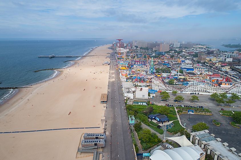 Aerial view of Coney Island, showing the beach, boardwalk, amusement park rides, and surrounding urban landscape