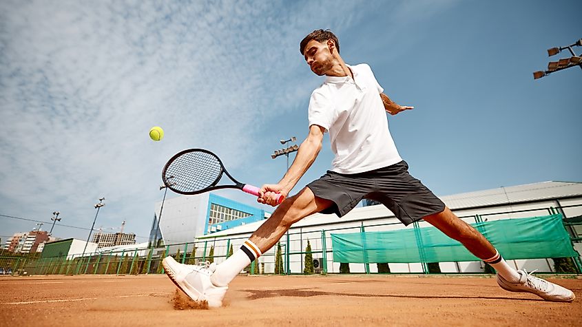 Dynamic image of focused man playing tennis on outdoor clay court.