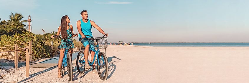 A couple enjoying a Florida beach vacation, biking near the Sanibel Island Lighthouse at sunset.