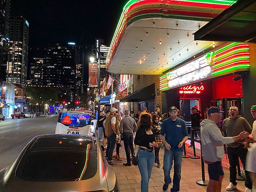 The evening crowd outside of the red and green lights of the Comedy Mothership, backdropped by the rest of spritely Sixth Street in Austin.