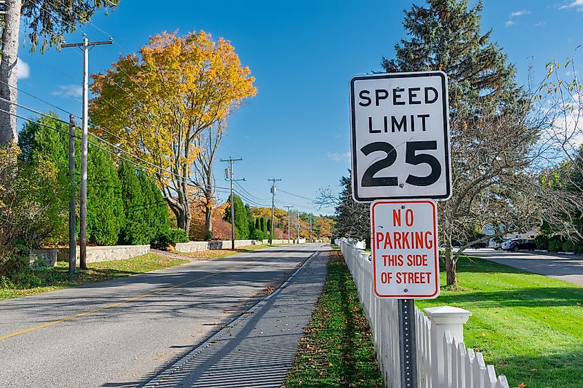 Traditional American speed limit and no parking signs above a white picket fence on Ocean Ave in Kennebunkport, Maine.