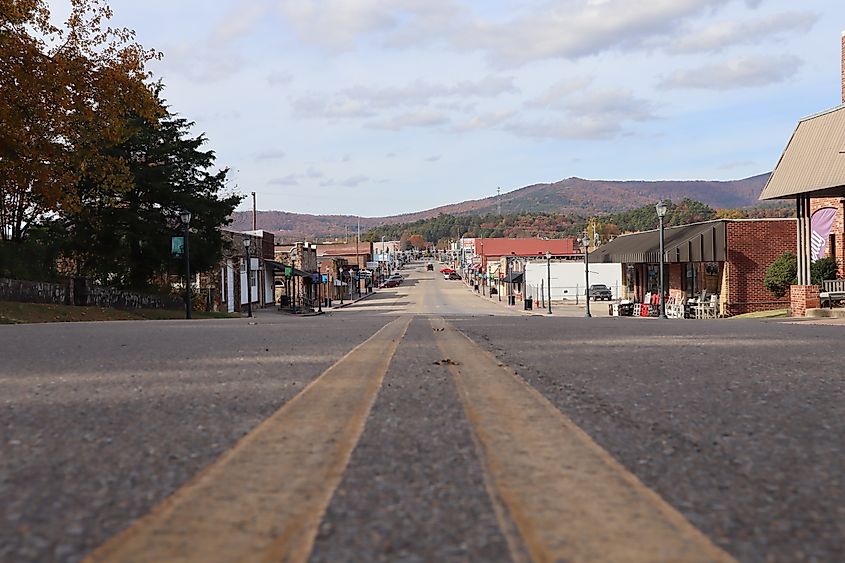 Street-level view down Main Street (Mena Street) in Mena, Arkansas, with autumn colors on Rich Mountain in the background, capturing the essence of small-town America.