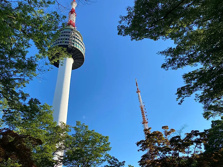 Two radio towers spike into a blue sky through the trees.