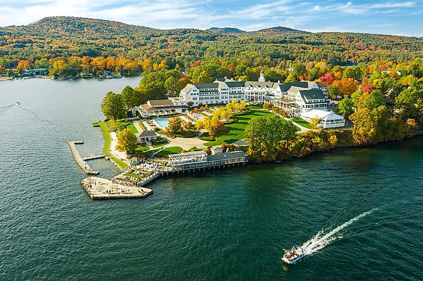 Autumnal foliage blankets the shores of Lake George as the sun sets, captured from aerial perspectives by a drone.