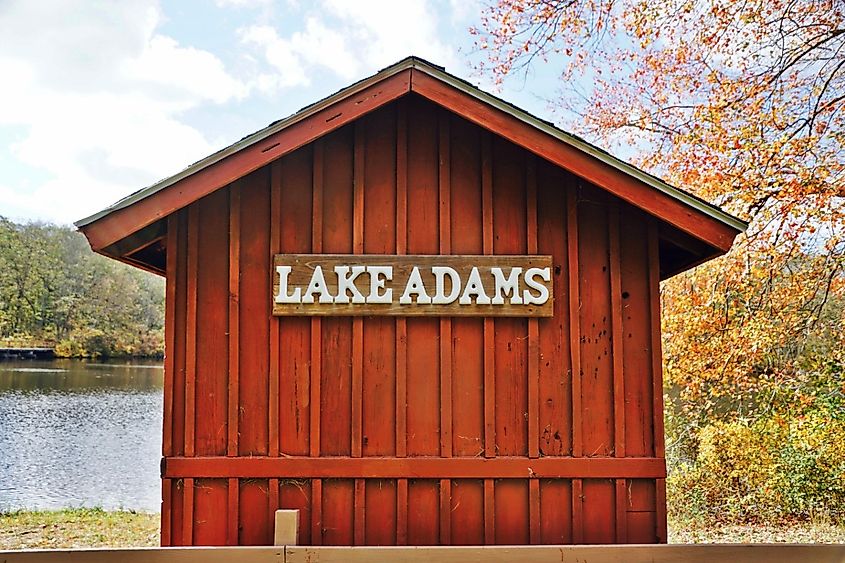 A horizontal image of a red wooden boat house overlooking a freshwater pond.