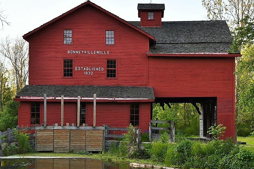 Daytime photo of the red barn mill at Bonneyville Mills in Bristol, Indiana with a calm pond and reflection in the foreground