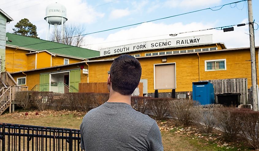 Young male visitor stands in front of Big South Fork Scenic Railroad station in the historical coal mining town of Stearns, Kentucky, USA