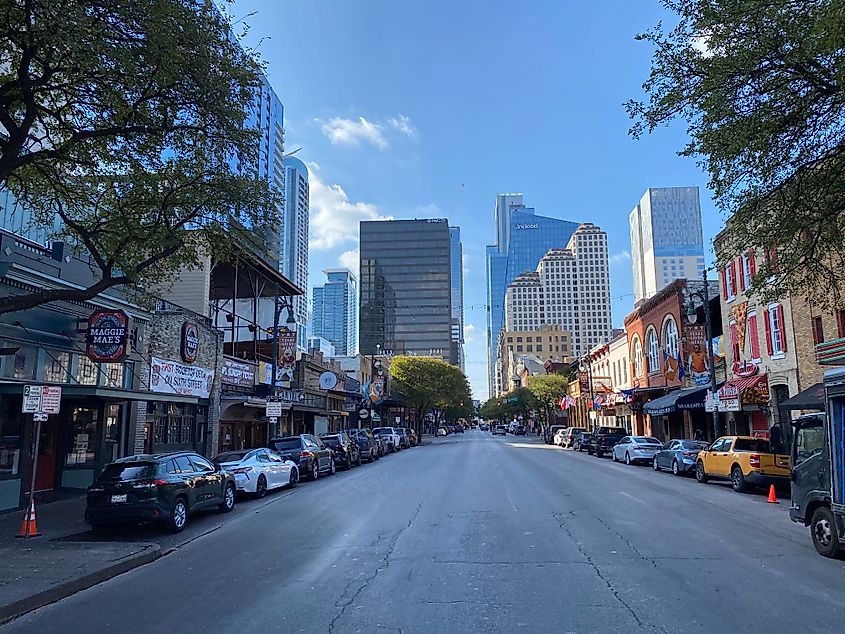 The scrappy businesses of Austin's 6th Street are backdropped by glass skyscrapers, which themselves are backdropped by a bluebird sky.  