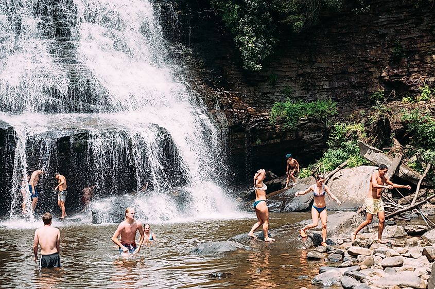 Tourists and visitors swimming beneath the waterfall at Swallow Falls State Park in Oakland, Maryland.