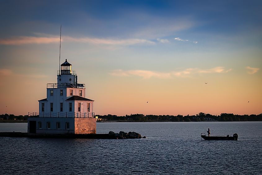 A fisherman in his boat casts his line at sunrise by the Lake Michigan lighthouse, Manitowoc, Wisconsin.