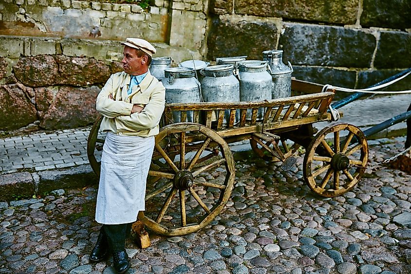 A milkman is standing next to a cart with milk. Image by Vladfotograf via Shutterstock.com