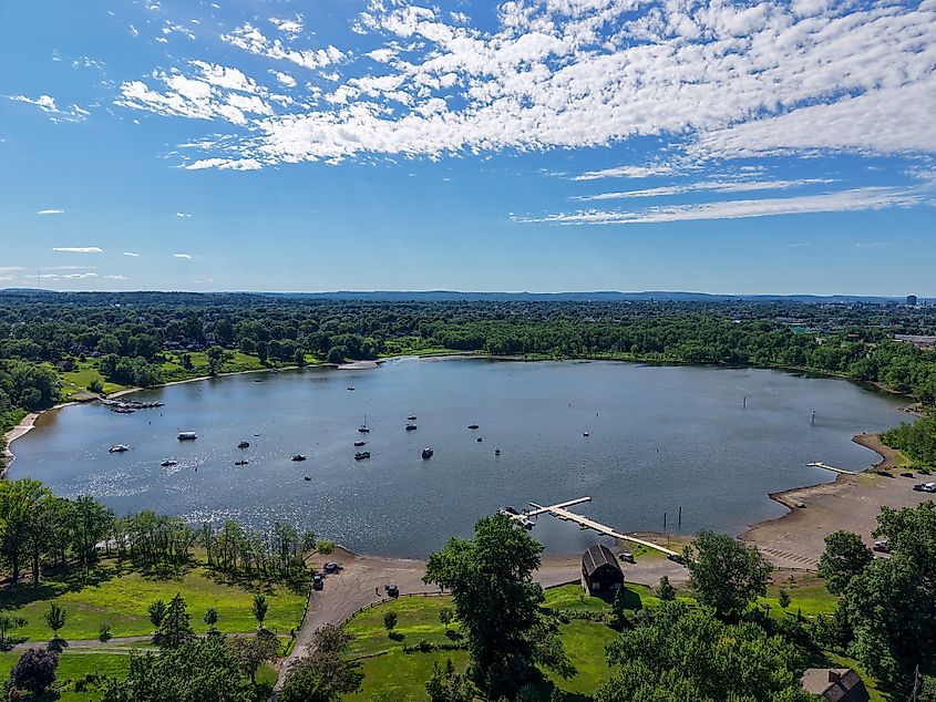 Aerial view of Wethersfield Cove in Connecticut showing small boats on the water, a dock, shoreline, and expansive greenery under a partly cloudy sky.