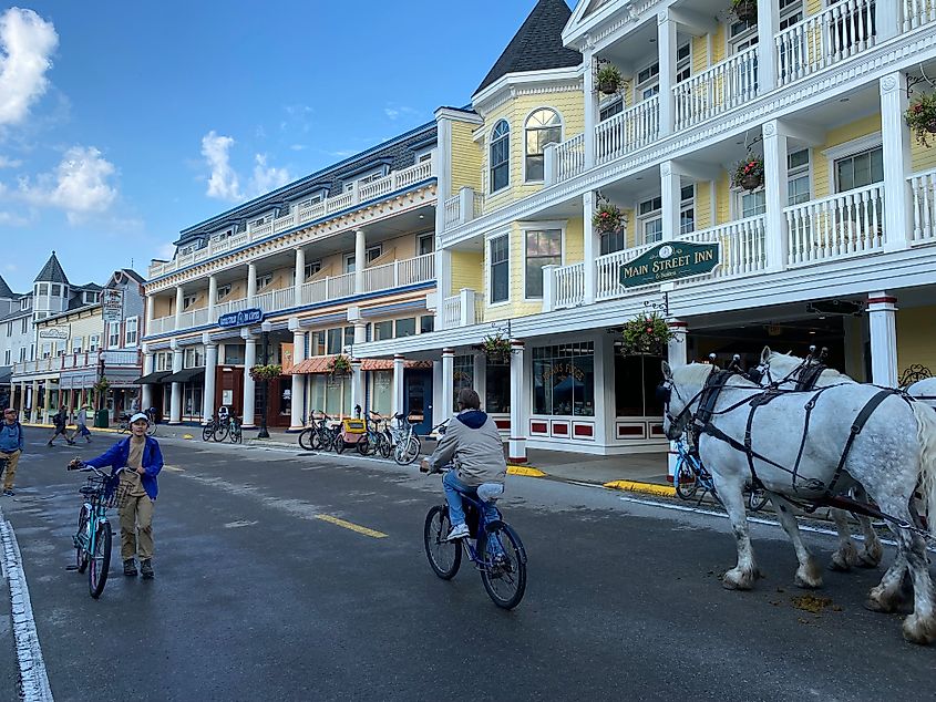 Cyclists share a car-free road with working horses. An elegant inn and other lightly-colored Victorian buildings line the street