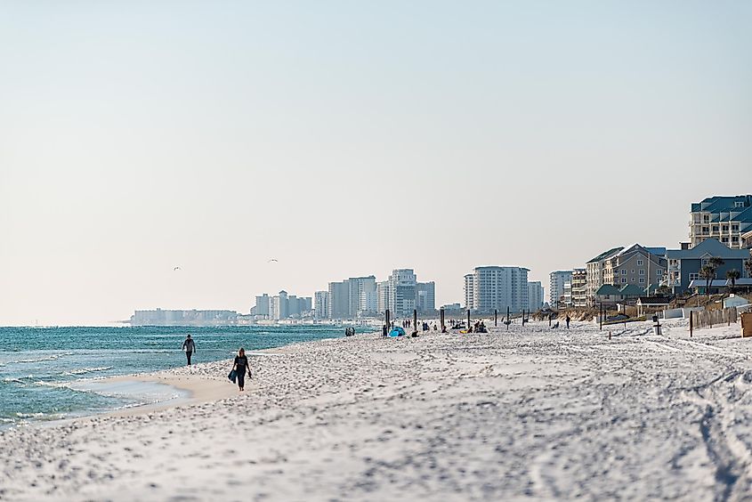 Scenic view of Miramar Beach with people walking along the shore, buildings in the distance, near Destin, Florida.