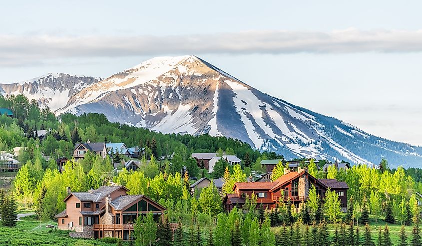 Mount Crested Butte, Colorado village in summer with colorful sunrise by wooden lodging houses on hills with green trees