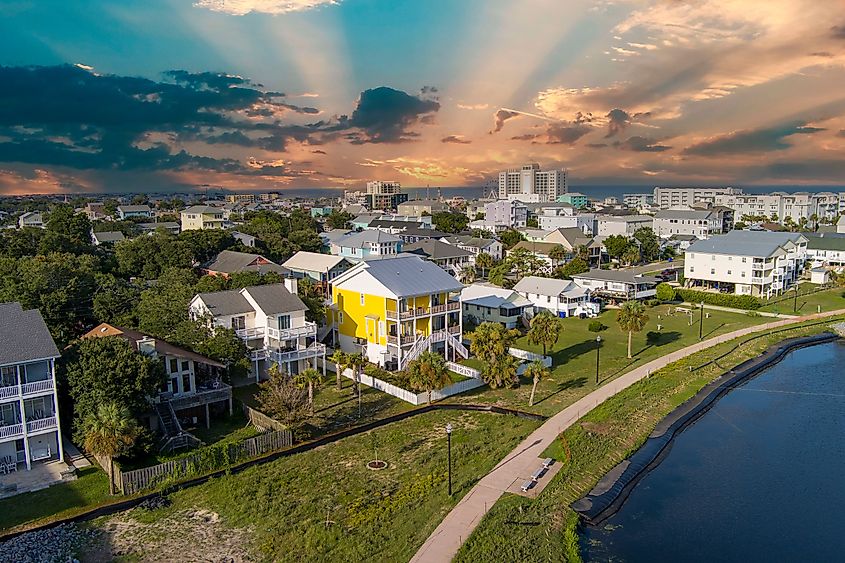 Aerial view of homes along the shores of Carolina Lake with hotels, retail stores, and apartments in the city skyline, powerful clouds at sunset, and the Atlantic Ocean in Carolina Beach, North Carolina