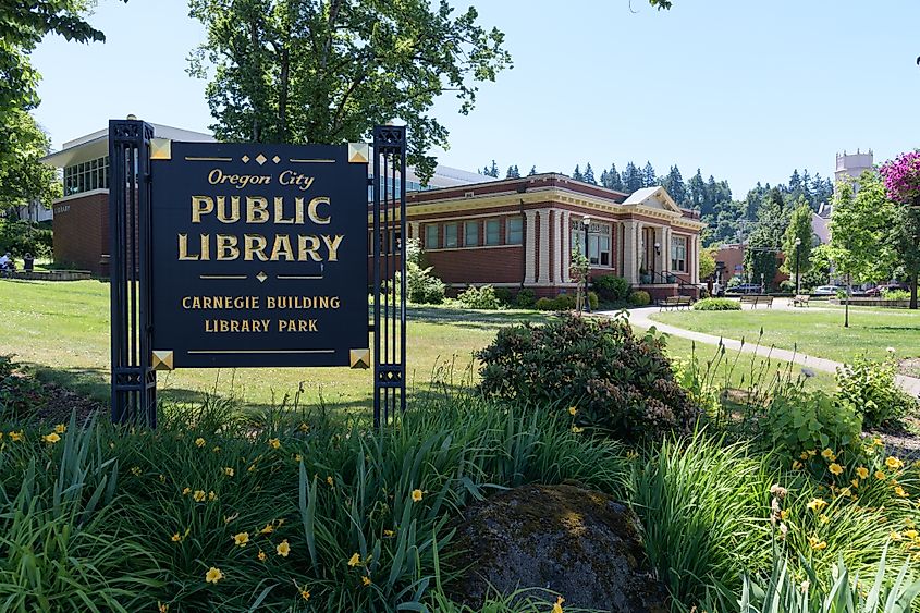 Sign for the Oregon City Public Library with the historic Carnegie Building in the background, located in Library Park, Oregon City, Oregon.