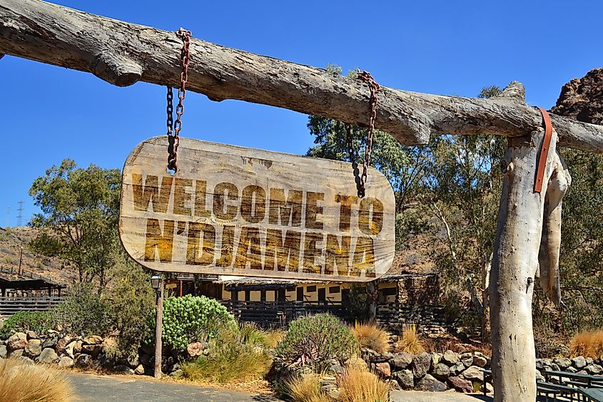 Old vintage wood signboard with text "welcome to N'djamena" hanging on a branch.