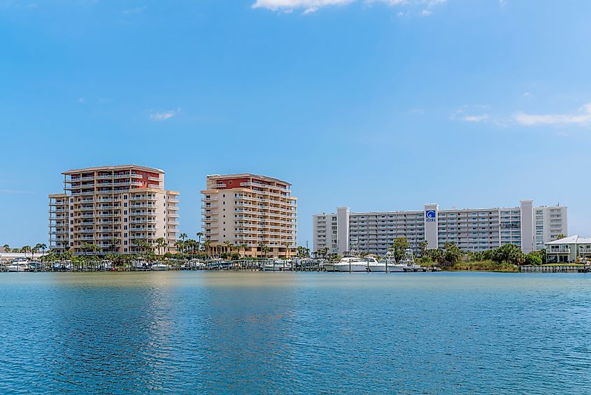 Hotels and apartments along scenic Destin Harbor in Destin, Florida, featuring waterfront vacation rental condominium units with beautiful views of the sea against a blue sky.