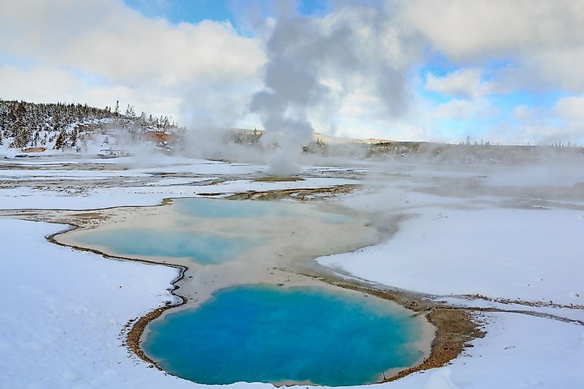 Geysers emitting steam in the snow-covered landscape of Yellowstone National Park in winter.